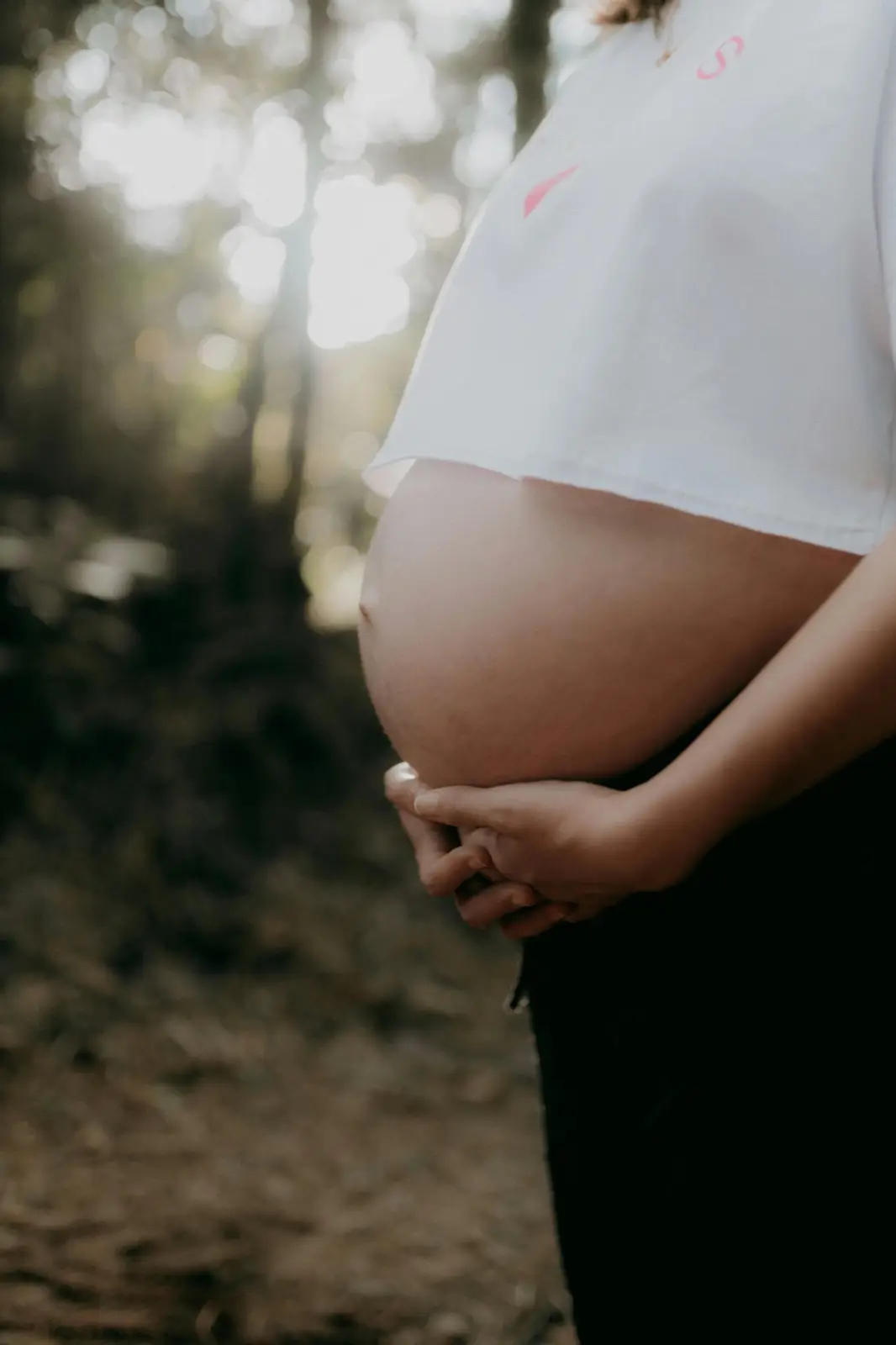 Femme enceinte sereine en forêt, mains posées sur son ventre